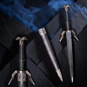 May include: Three fantasy swords with silver accents and black handles and sheaths are displayed on a dark background. The swords have ornate pommels and crossguards. One sword is unsheathed, revealing a silver blade.