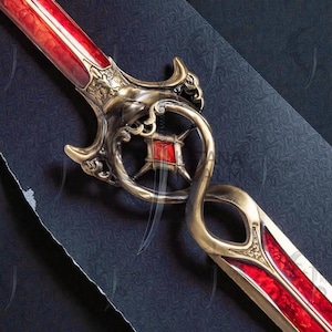 Puede incluir: Espada ornamentada con una hoja roja y una empuñadura dorada. La empuñadura presenta un diseño decorativo con una gema roja central y detalles intrincados. La hoja tiene una superficie roja texturizada con una línea blanca central.