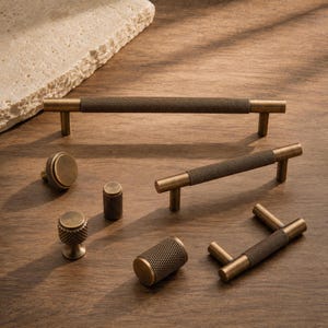 May include: A collection of antique brass cabinet hardware, including knobs and pulls. The hardware features a textured, knurled design on the handles and knobs, with a warm, golden-brown finish. The hardware is arranged on a wooden surface.