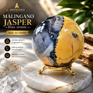 Puede incluir: Una esfera de jaspe Malingano pulida con un patrón bicolor de gris carbón profundo y amarillo mostaza vibrante, sobre un soporte de trípode de metal dorado. El texto en la imagen dice ARROWHEADHUB MALINGANO JASPER RARE SPHERE SIZE: 45-50MM.