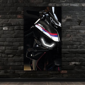 Puede incluir: Primer plano de una motocicleta negra y plateada con faros blancos brillantes. La motocicleta tiene un acabado de fibra de carbono con detalles en rojo, blanco y azul. La imagen está montada en una pared de ladrillo oscuro.