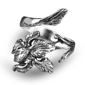 Puede incluir: Un anillo plateado con un diseño floral. El anillo se envuelve alrededor del dedo con una flor detallada en el centro y detalles en forma de hojas. El anillo está sobre un fondo blanco.