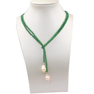 May include: A green beaded necklace with a Y-shaped design. The necklace features two strands of small, round green beads that meet at a knot. Two large, teardrop-shaped, light pink pearls dangle from the bottom.