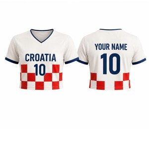 May include: White Croatia soccer jersey with a V-neck and navy blue trim. The front displays "CROATIA" and the number "10" in navy blue, above a red and white checkered pattern. The back features "YOUR NAME" and the number "10".