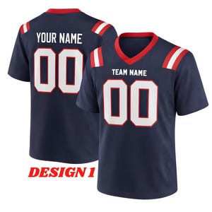 Puede incluir: Camiseta de f&uacute;tbol azul marino con n&uacute;meros blancos y detalles en rojo y blanco. La camiseta tiene el texto "TEAM NAME" y "YOUR NAME" impresos, junto con el n&uacute;mero "00". El dise&ntilde;o est&aacute; etiquetado como "DESIGN 1".