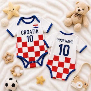 May include: Two white baby onesies with blue trim and a red and white chequered pattern. One has "CROATIA 10" and the Croatian flag. The other says "YOUR NAME 10". Baby toys, including a teddy bear, surround the onesies.