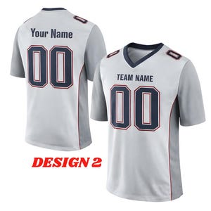 Puede incluir: Dos camisetas de f&uacute;tbol gris claro con el n&uacute;mero "00" en azul marino con un contorno rojo. Una camiseta tiene "Your Name" en la espalda, la otra tiene "TEAM NAME" en la parte delantera. El texto "DESIGN 2" tambi&eacute;n es visible.