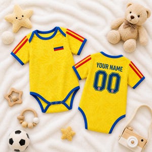 May include: Two yellow baby onesies with blue trim and red stripes on the sleeves. One has a small pocket with a flag design, the other has "YOUR NAME" and the number "00" on the back. The onesies are surrounded by baby toys.