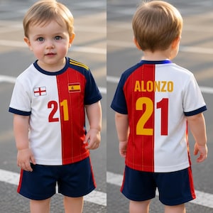 May include: A toddler wearing a white, red, and navy blue soccer jersey and shorts. The jersey has the number 21 in yellow and red, and the name "ALONZO" on the back. The jersey also features the flags of England and Spain.
