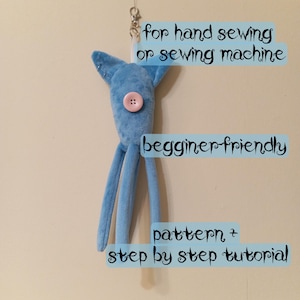 Puede incluir: Una criatura de peluche azul claro con largas piernas y un botón rosa. El texto "for hand sewing or sewing machine", "beginner-friendly" y "pattern + step by step tutorial" se muestra en la imagen. Un cierre plateado está adjunto en la parte superior.