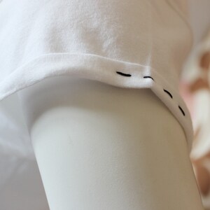 May include: Close-up of a white t-shirt sleeve with black stitching along the edge.