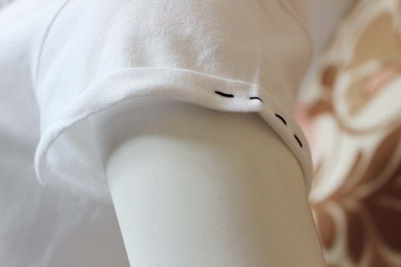 May include: Close-up of a white t-shirt sleeve with black stitching along the edge.