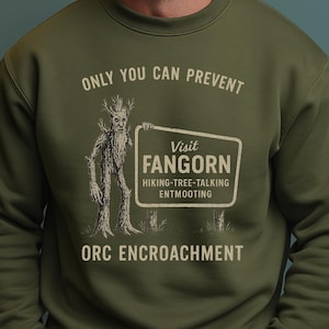 May include: Olive green sweatshirt with the text "ONLY YOU CAN PREVENT ORC ENCROACHMENT." The design includes a tree-like figure holding a sign that reads "Visit Fangorn, Hiking-Tree-Talking Entmooting."