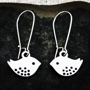 May include: A pair of silver bird-shaped earrings. Each earring has a bird silhouette with a small eye and a series of dots on the belly. The earrings have long, curved hooks for pierced ears.
