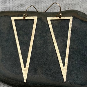 May include: A pair of gold triangle earrings with a textured finish. The earrings are simple and modern in design.