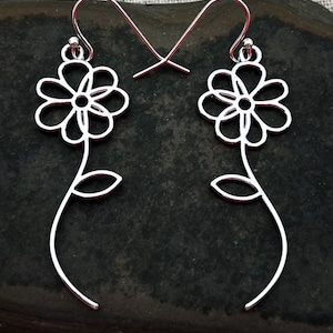 May include: A pair of silver dangle earrings featuring a delicate flower design with a stem and leaf. The earrings are made of wire and have a simple, minimalist style.