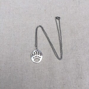 May include: A silver necklace with a bear paw pendant. The pendant is a cutout design of a bear paw print.