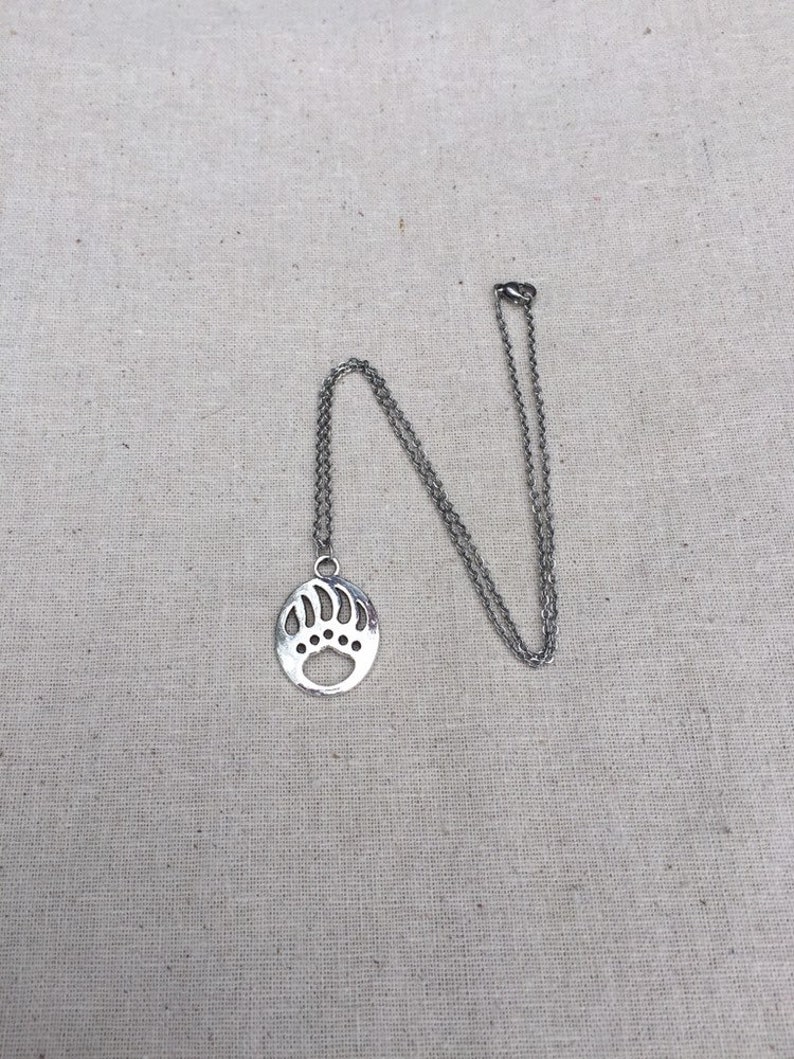 May include: A silver necklace with a bear paw pendant. The pendant is a cutout design of a bear paw print.