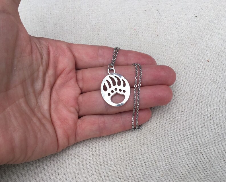 May include: A silver necklace with a bear paw print pendant. The pendant is a circle with a cut-out bear paw print.