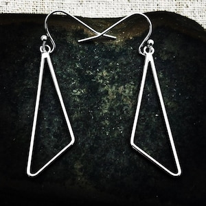 May include: A pair of silver-colored, geometric earrings. Each earring features a triangular shape with a hook for the ear. The earrings are made of a shiny, metallic material and are displayed against a dark background.