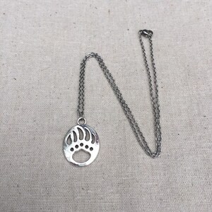May include: A silver chain necklace with a circular pendant featuring a bear paw print design.