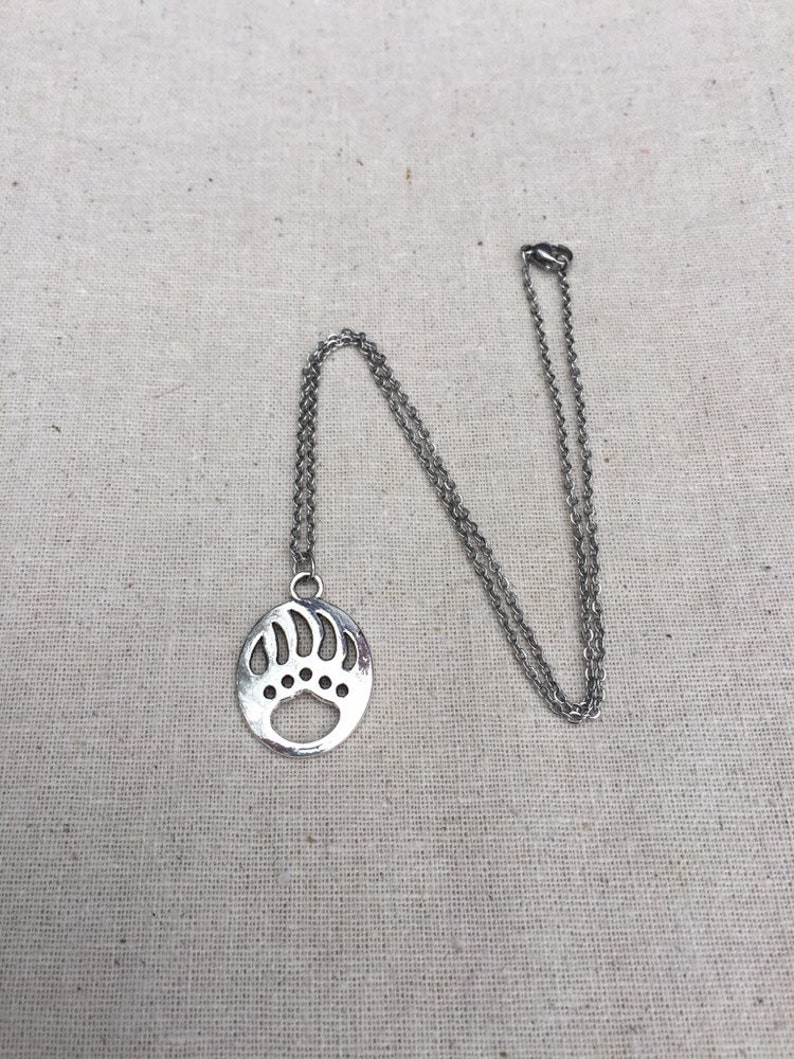 May include: A silver chain necklace with a circular pendant featuring a bear paw print design.