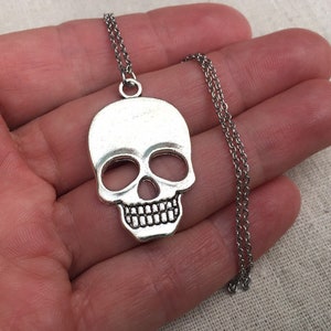 May include: Silver skull pendant necklace with a silver chain. The skull is detailed with eye sockets, a nose, and teeth.