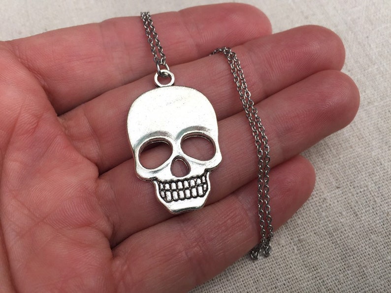 May include: Silver skull pendant necklace with a silver chain. The skull is detailed with eye sockets, a nose, and teeth.