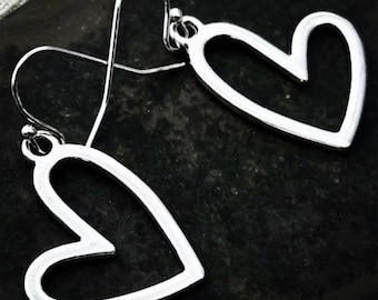 May include: A pair of silver heart-shaped dangle earrings. The earrings have a simple, open heart design and are suspended from a hook. The earrings are displayed against a dark, textured background.