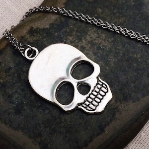 May include: A silver skull pendant necklace with a chain. The skull is detailed with eye sockets, a nose, and a mouth with teeth.
