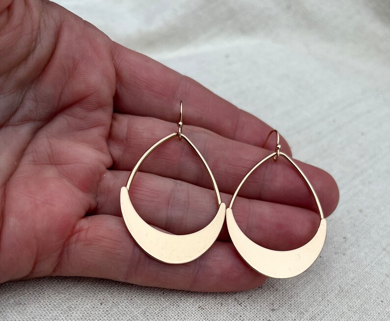 Puede incluir: Un par de pendientes colgantes de color dorado con forma de media luna. Los pendientes est&aacute;n hechos de metal y tienen un dise&ntilde;o simple y moderno.