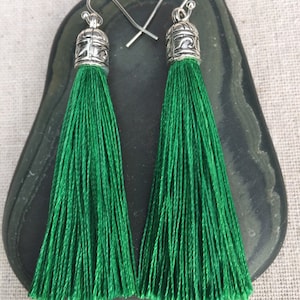 May include: A pair of green tassel earrings with silver metal tops. The tassels are long and have a fringe-like appearance.
