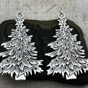 Könnte beinhalten: Ein Paar silberfarbene Ohrringe in Form eines Weihnachtsbaums. Die Ohrringe sind aus Metall und haben ein detailliertes Design. Sie sind perfekt, um jedem Outfit eine festliche Note zu verleihen.