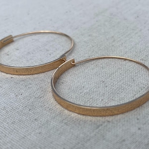 May include: A pair of gold hoop earrings. The earrings are simple and elegant, with a smooth, polished finish.