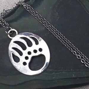 May include: A silver necklace with a bear paw print pendant. The pendant is a circle with a detailed outline of a bear paw print.