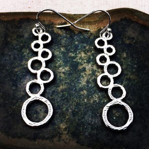 May include: A white ceramic mug with a black handle and the text "But First, Coffee" in a black, handwritten-style font. The mug is on a white surface.