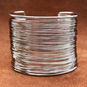 May include: A silver bangle bracelet made of multiple thin wires wrapped around each other. The bracelet is open and has a simple design.