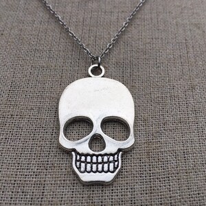 May include: A silver skull pendant necklace. The skull is detailed with eye sockets, a nose, and a toothy grin.