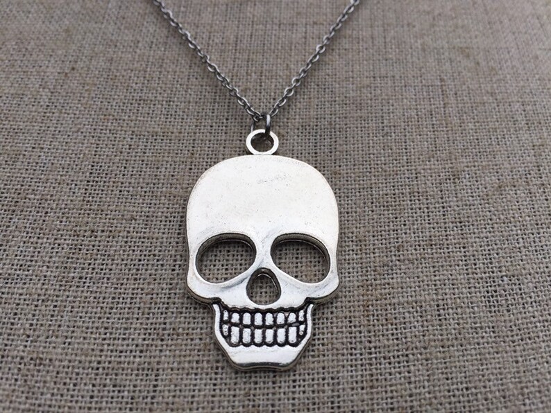 May include: A silver skull pendant necklace. The skull is detailed with eye sockets, a nose, and a toothy grin.