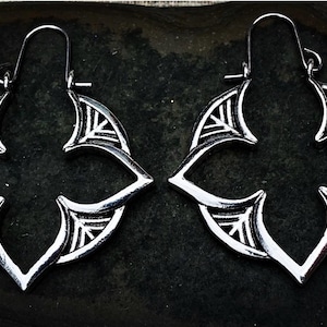 May include: A pair of silver-toned hoop earrings featuring a four-pointed star or floral cutout design with etched line details. The earrings have a hinged wire closure at the top, creating a symmetrical shape with pointed edges.