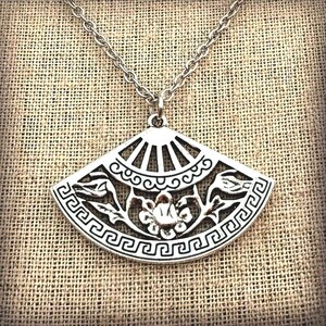 May include: Silver-toned pendant necklace featuring a fan-shaped design. The pendant has intricate cut-out details of floral and geometric patterns. The necklace hangs on a delicate chain, perfect for adding a touch of elegance to any outfit.