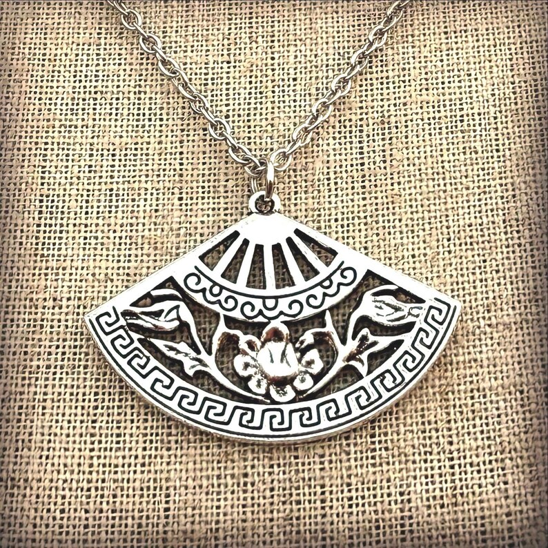 May include: Silver-toned pendant necklace featuring a fan-shaped design. The pendant has intricate cut-out details of floral and geometric patterns. The necklace hangs on a delicate chain, perfect for adding a touch of elegance to any outfit.