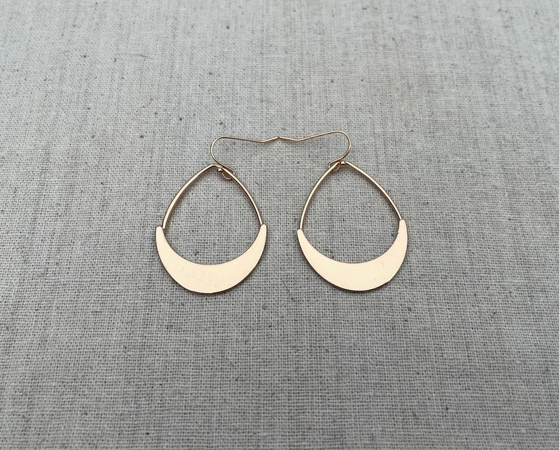 Puede incluir: Un par de pendientes de color dorado con forma de media luna. Los pendientes son simples y elegantes.