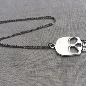 May include: A silver skull pendant necklace with a chain. The skull has a detailed design with eye sockets and teeth.