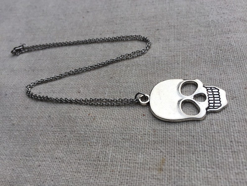 May include: A silver skull pendant necklace with a chain. The skull has a detailed design with eye sockets and teeth.