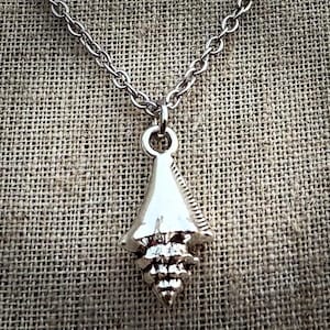 May include: A silver-toned metal pendant shaped like a stylized arrowhead or seashell, suspended from a matching silver-toned metal link chain. The pendant features a smooth, triangular upper section and a textured, ridged lower section.