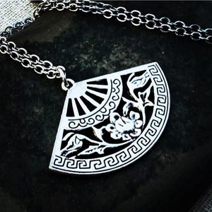 May include: Silver-toned pendant necklace featuring a fan-shaped design. The pendant showcases a detailed floral and geometric pattern with a sunburst design. The necklace has a delicate chain.