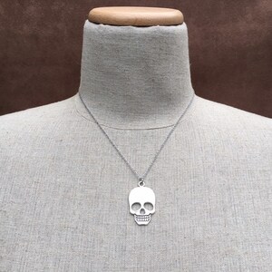 May include: A silver skull pendant necklace on a mannequin. The pendant is a simple, flat design with no details.