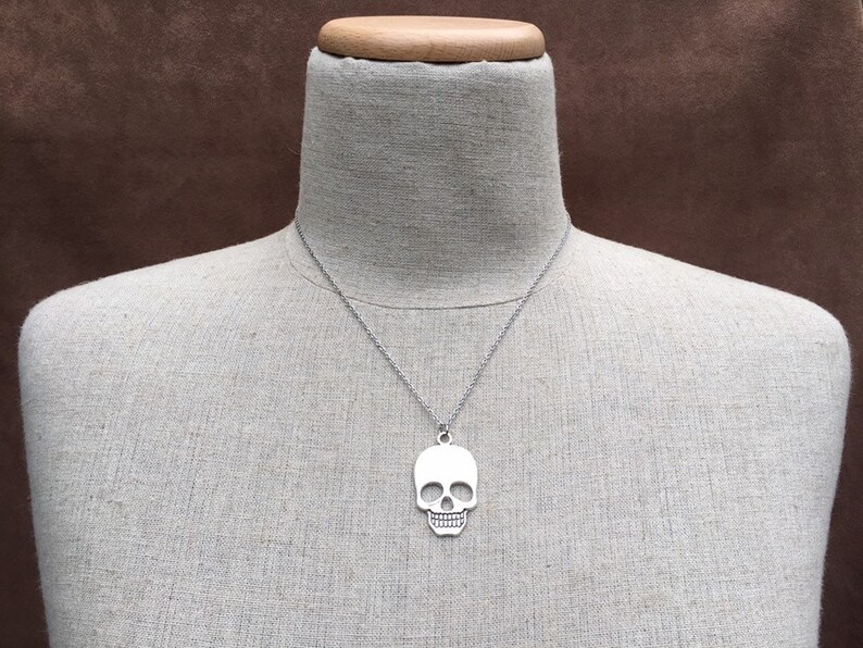 May include: A silver skull pendant necklace on a mannequin. The pendant is a simple, flat design with no details.
