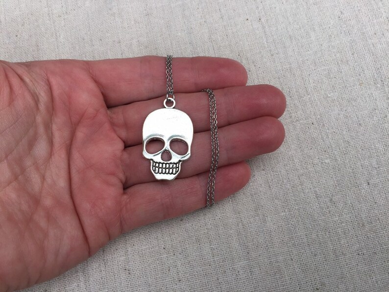 May include: A silver skull pendant necklace with a delicate chain. The skull is detailed with eye sockets, a nose, and a mouth.